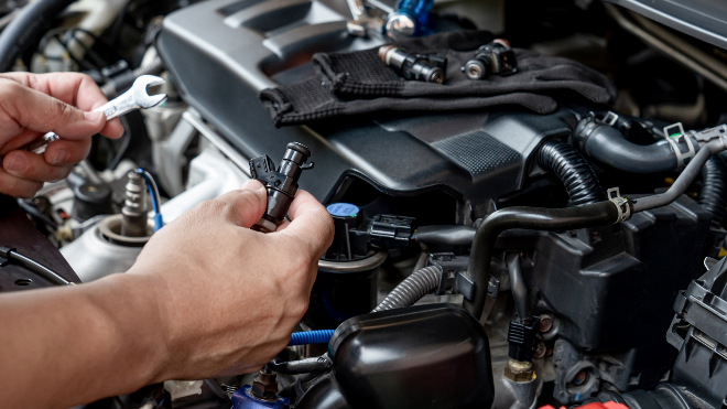 Technician holding a wrench and a DPF sensor above an engine.