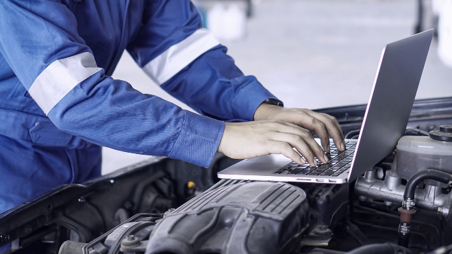 Delphi expert using a laptop which is resting on top of the exposed engine of a vehicle.