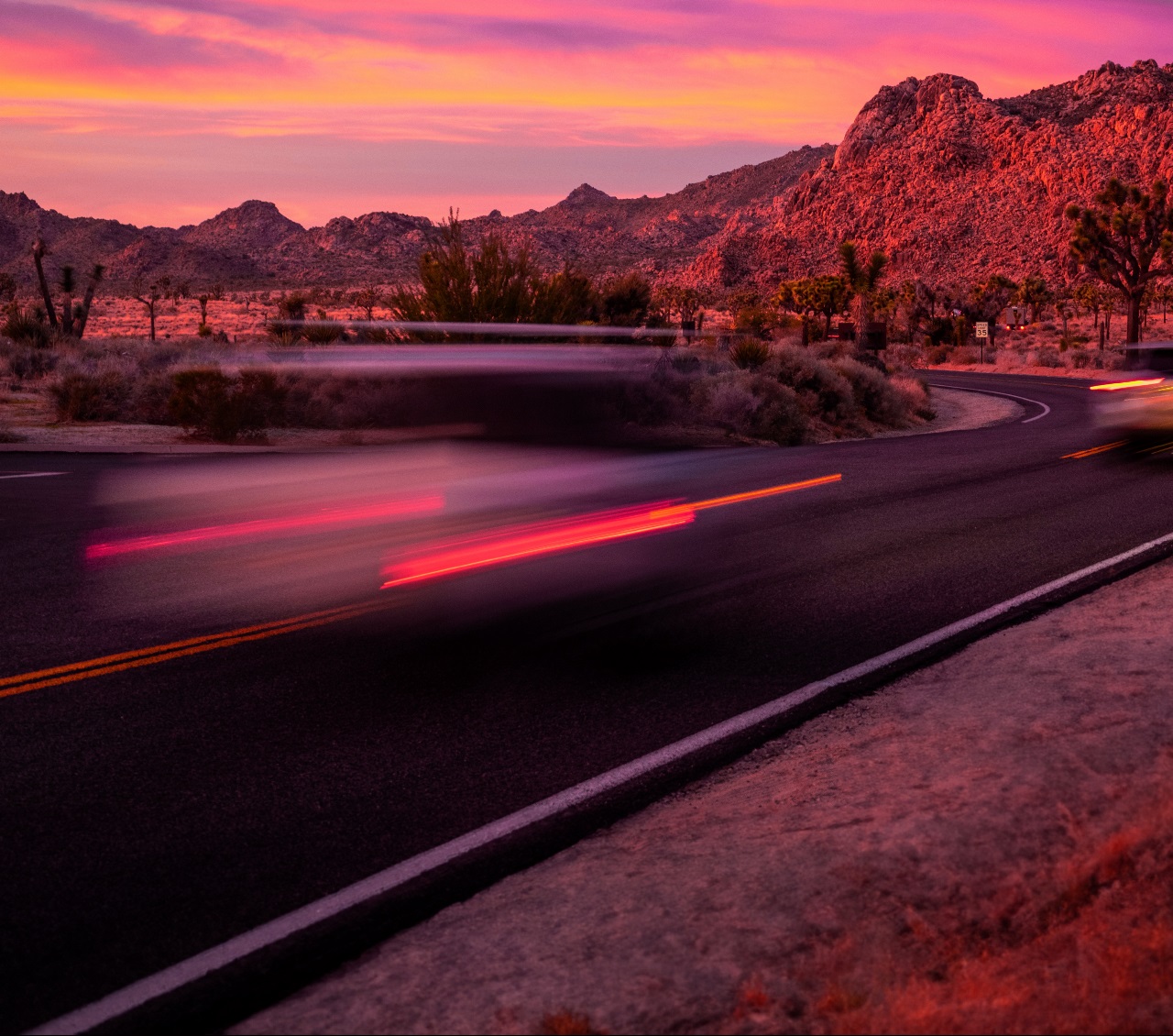 A winding road with a car traveling quickly during sunset